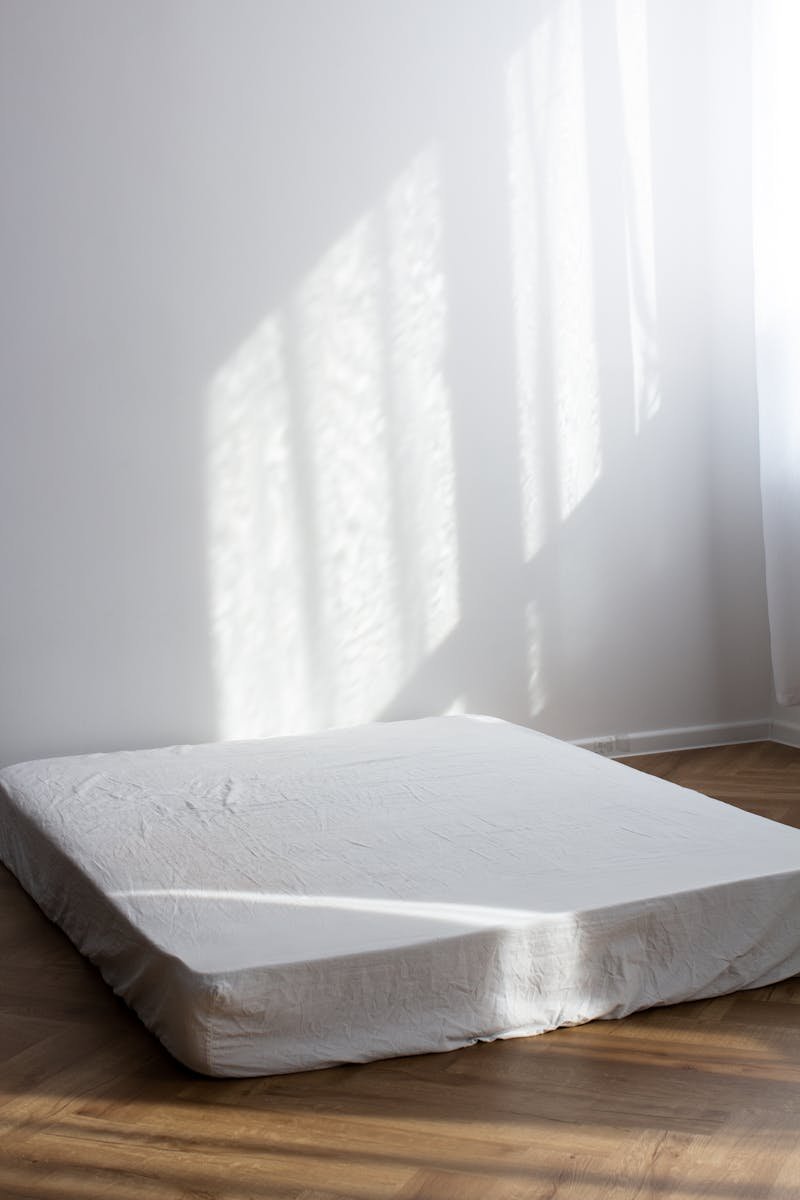 Photo by Alina Matveycheva A serene minimalist room with a sunlit mattress on a wooden floor, perfect for peaceful decors.