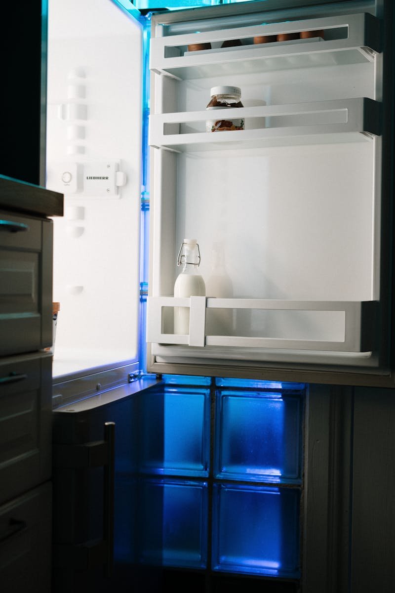 Photo by cottonbro studio An open refrigerator with minimal contents illuminated by neon light in a home kitchen.