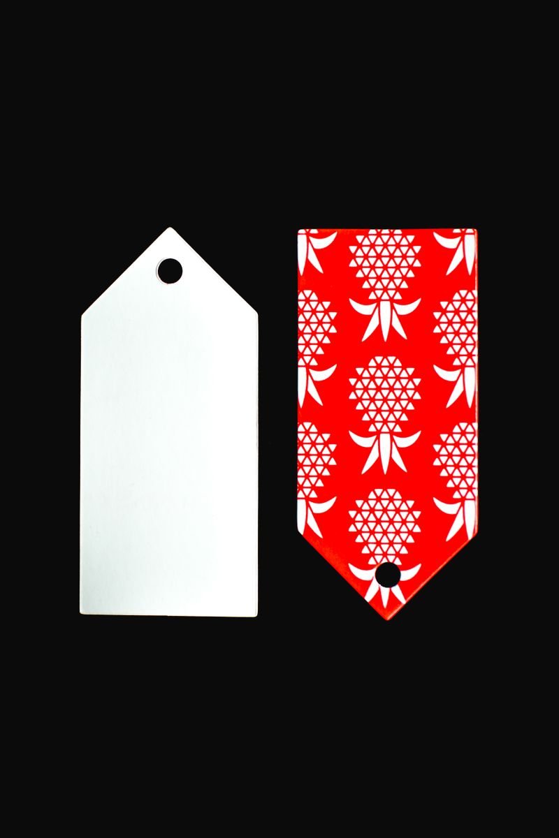 A close-up of two gift tags, one blank and the other with a pineapple pattern, on a black background.