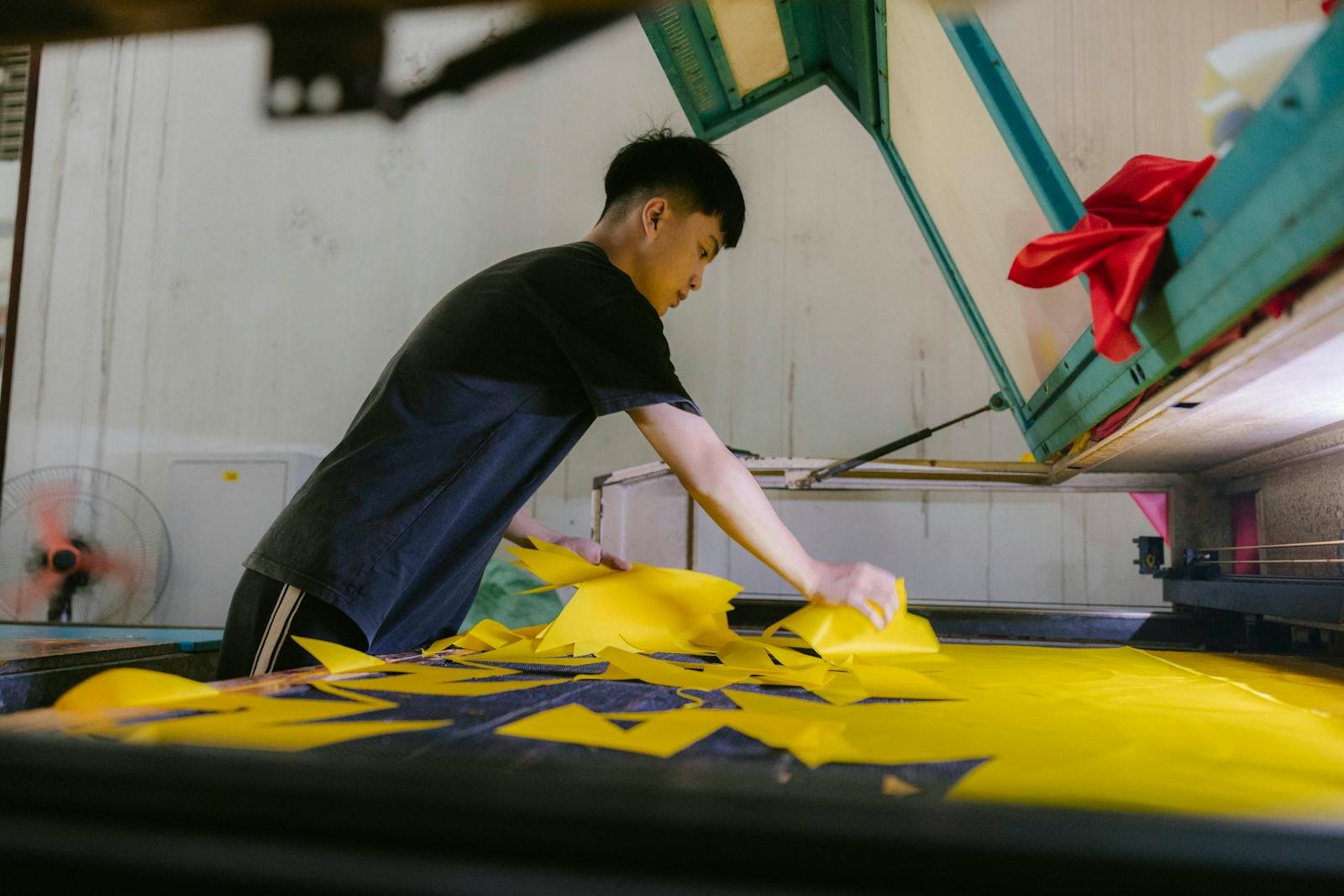 An adult man organizing yellow fabric pieces in an industrial factory setting indoors.